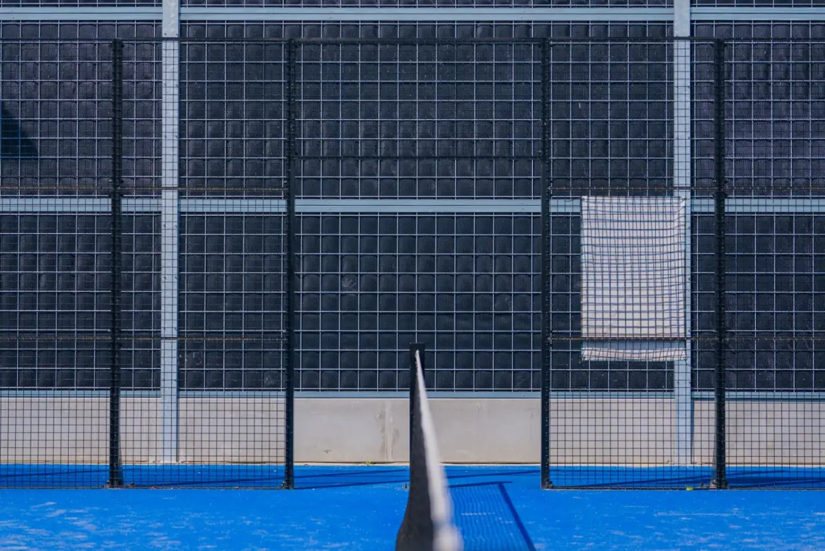 Noise-Reducer industrieel geluidsscherm rond een padelterrein, donkergrijze panelen achter de gaaswand